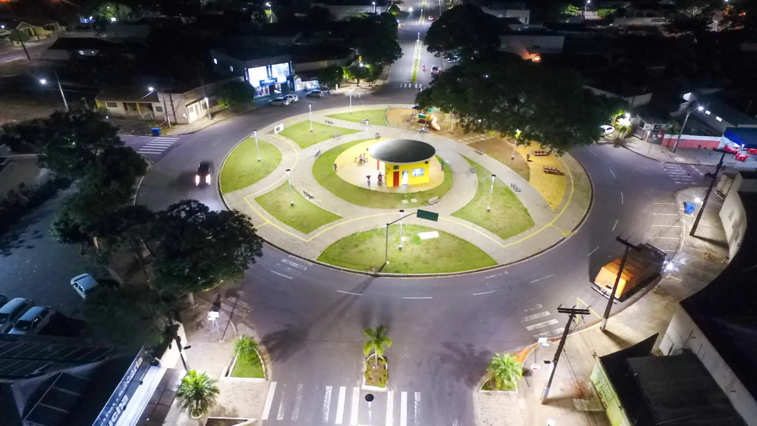 Vista aérea noturna de uma rotatória com praça central iluminada