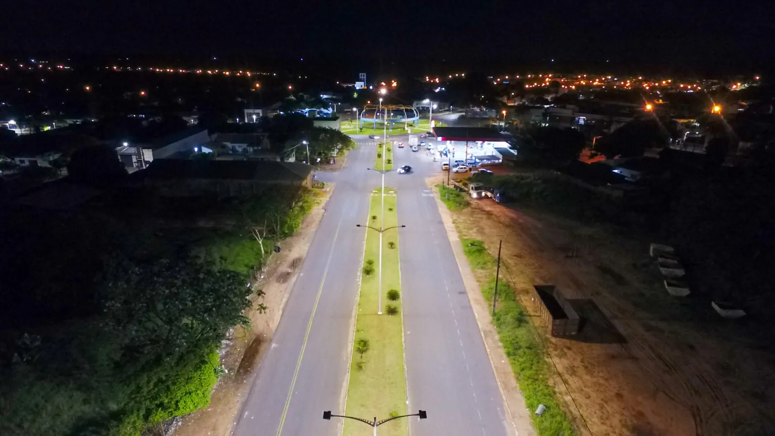 Vista aérea noturna de uma avenida com canteiro central iluminada por luminárias LED