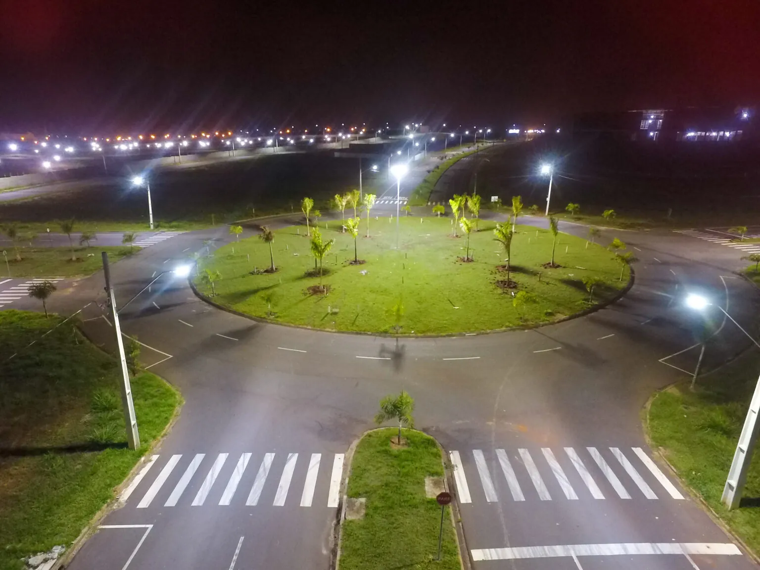 Vista aérea noturna de uma rotatória iluminada com faixas de pedestres